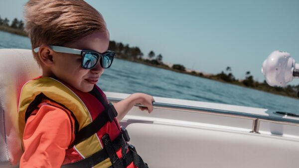 Blond boy wearing a life jacket and sunglasses sitting in a boat