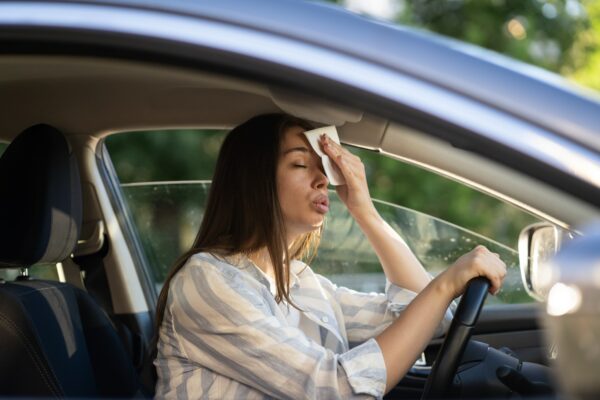 Woman driver being hot during heat wave in car, suffering from hot weather wipes sweat from forehead